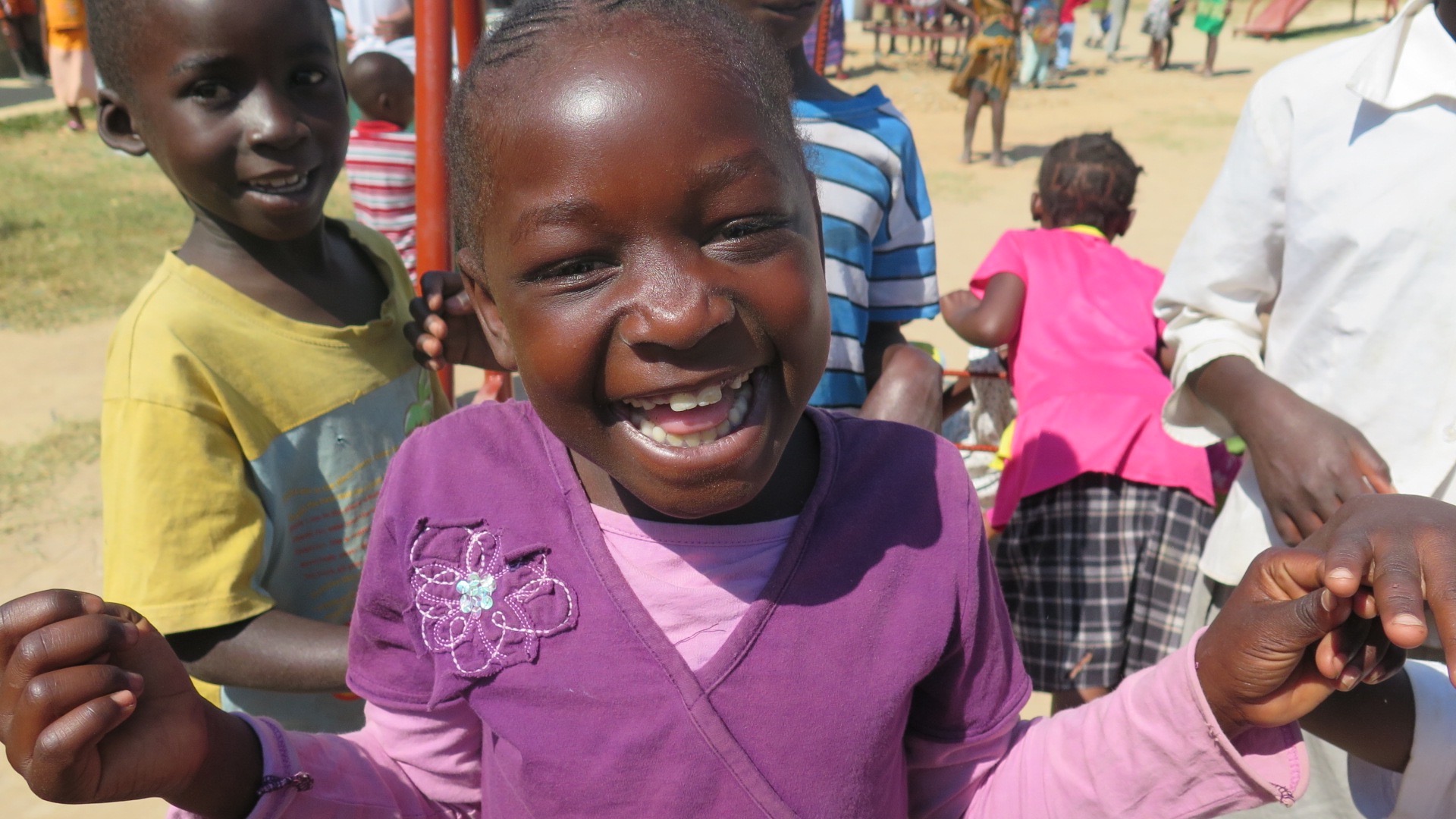 A young child in a purple sweater smiles in Zambia as others play behind her