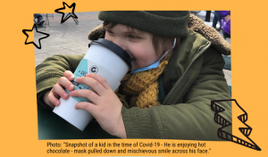 Photo: "Snapshot of a kid in the time of Covid-19 - He is enjoying hot chocolate - mask pulled down and mischievous smile across his face."