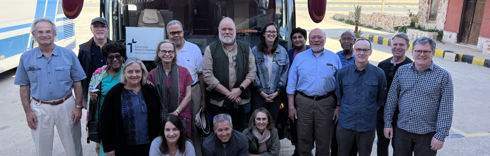 17 people stand in front of a bus posing for a photo