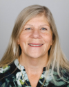 Headshot of a white woman wearing a green and black patterned shirt. She has blonde hair parted on the right side