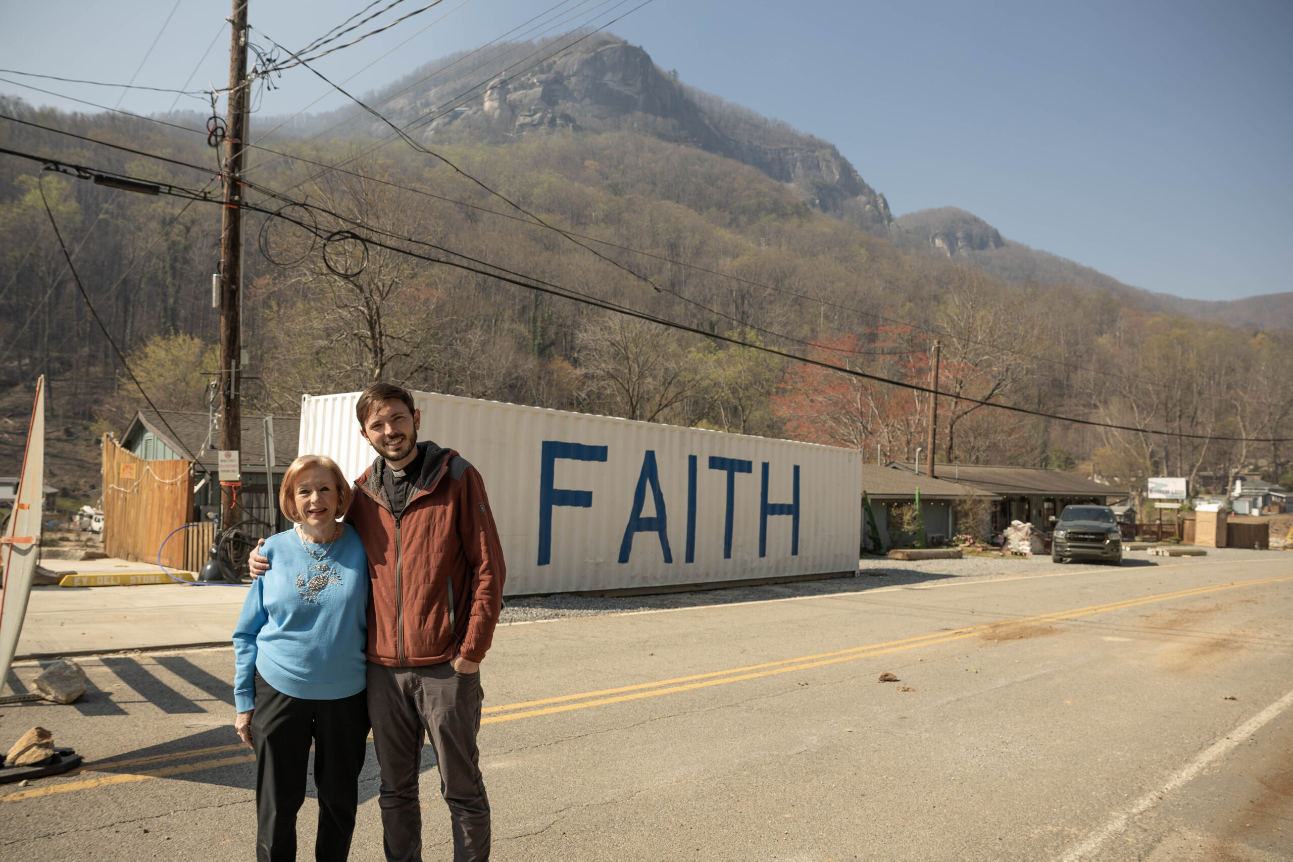 Linda and the Rev. John Roberts stand in front of a shipping container that reads “Faith.”